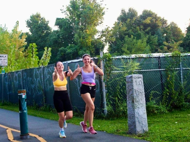 Two joyful women running past the one-mile marker in a park