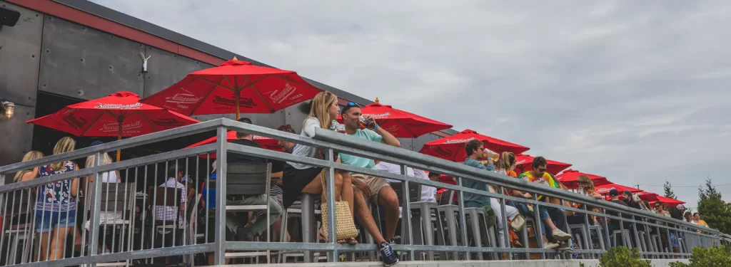 Visitors relax under red umbrellas on a brewery's outdoor deck